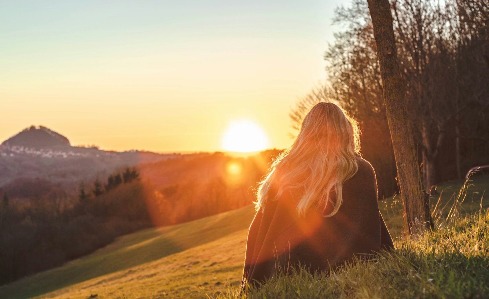 Woman sitting on a hillside facing the sunset